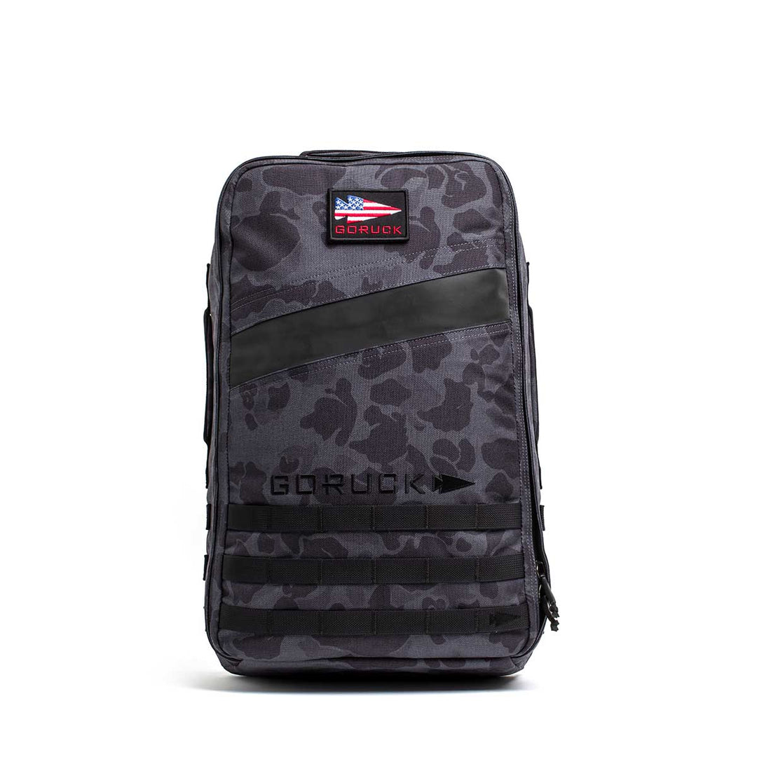The GORUCK Rucker 4.0 is a gray camo rucksack featuring a black patch, American flag badge, and "GORUCK" text on the front—perfectly built for rucking adventures.