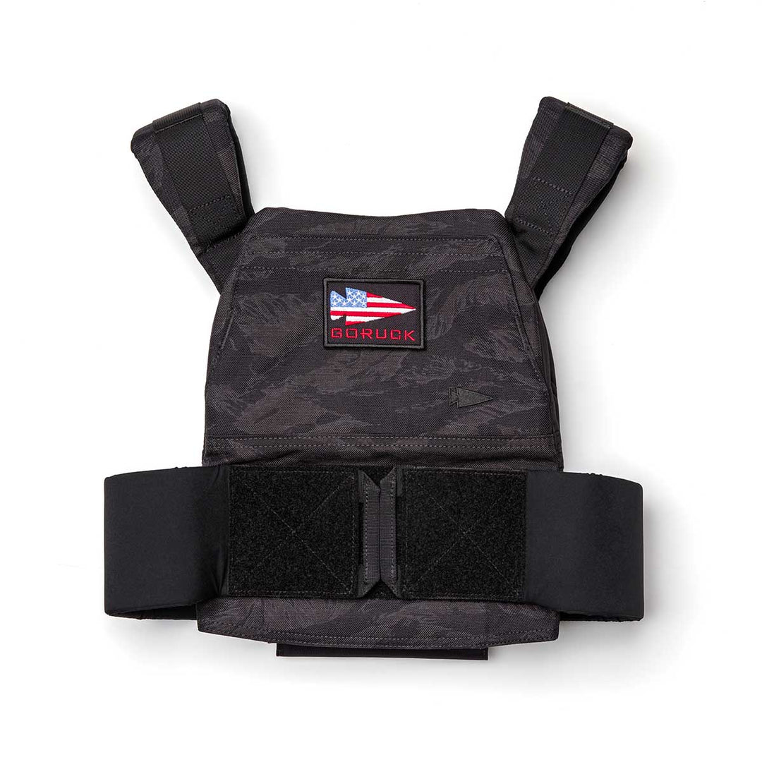 The Rucking Weight Vest features a black tactical design with an American flag and "GORUCK" patch on the front. It's perfect for rucking sessions and is compatible with Curved Ruck Plates for increased resistance.