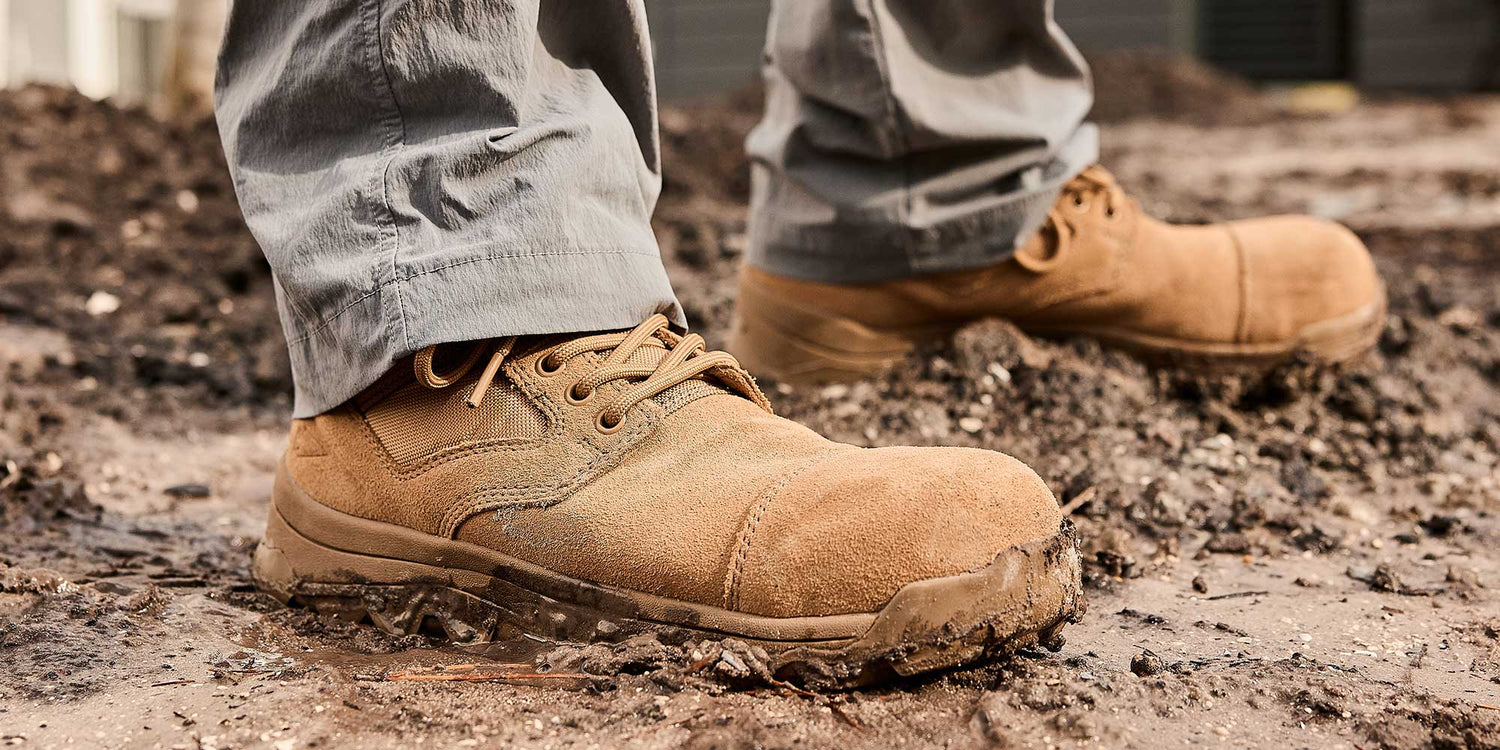 Close-up of a person wearing tan work boots standing on muddy ground.
