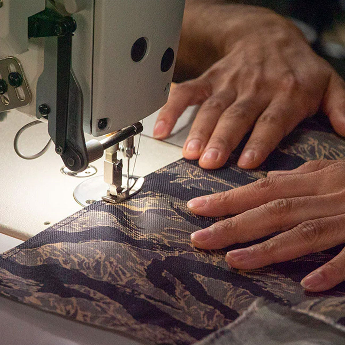 Close-up of hands guiding patterned fabric through a sewing machine.
