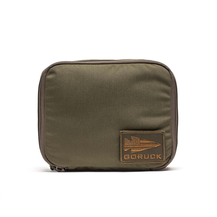 The GORUCK Shadow Pockets are olive green zippered pouches with a rectangular patch featuring the arrow logo on the front, perfect for efficient gear organization in your rucksack.