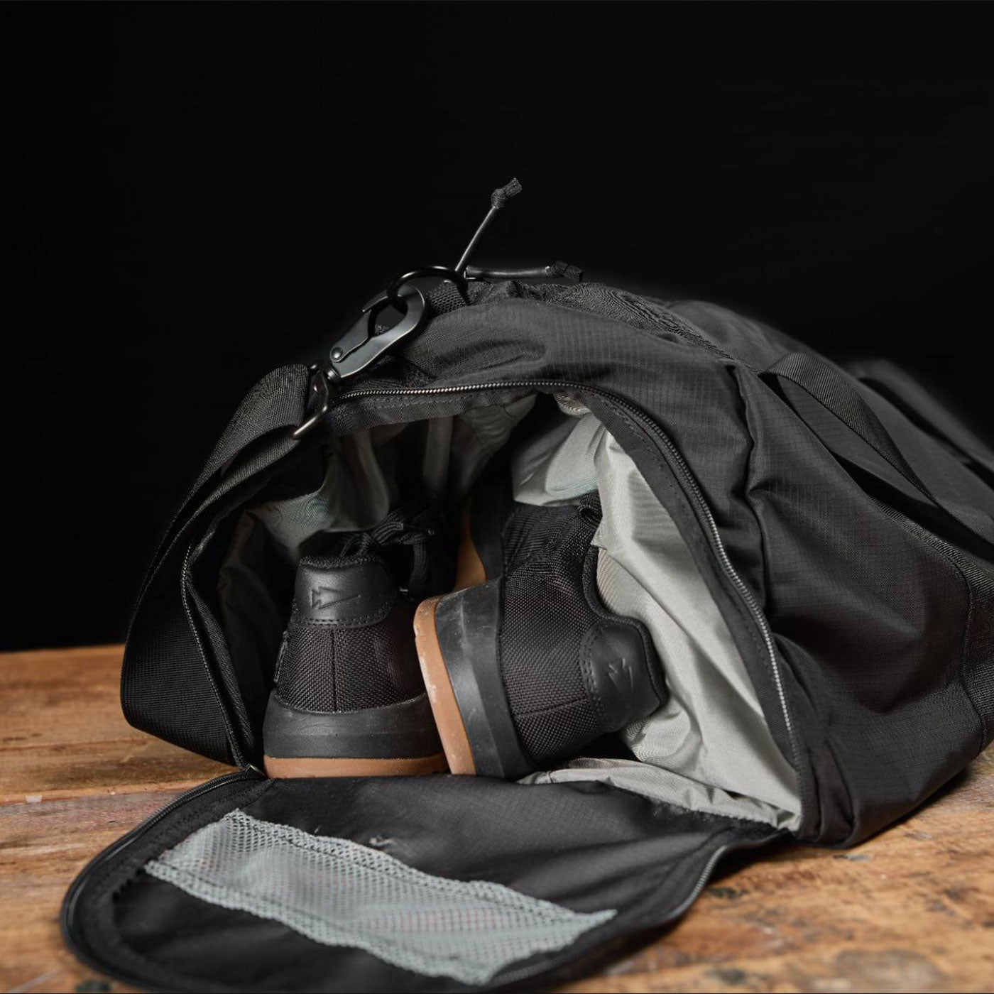 A black duffel bag with black sneakers partially packed inside, resting on a wooden surface.
