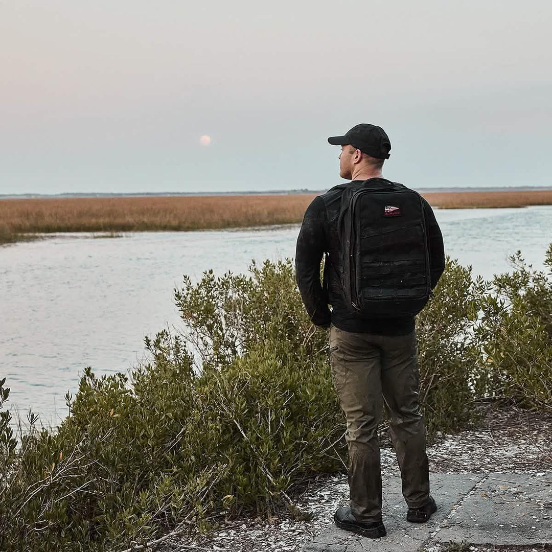Man wearing a GORUCK backpack by a marsh, outdoor adventure gear, rucking lifestyle.