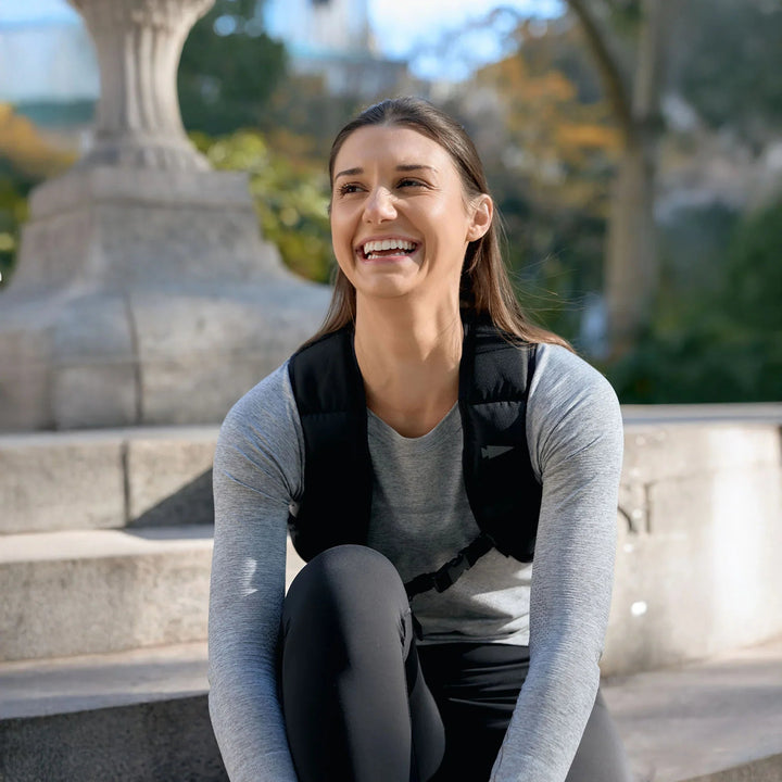 Woman wearing GORUCK rucking vest, smiling outdoors on stone steps in athletic gear