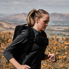 Woman rucking outdoors wearing GORUCK backpack and sternum pouch in a field of flowers.