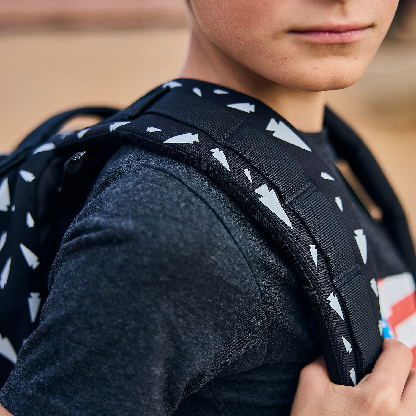 Close-up of a child wearing a black backpack with white arrow patterns, dressed in a dark t-shirt.