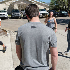 Man wearing GORUCK Subtle Spearhead Tee heather grey outdoors with group rucking gear