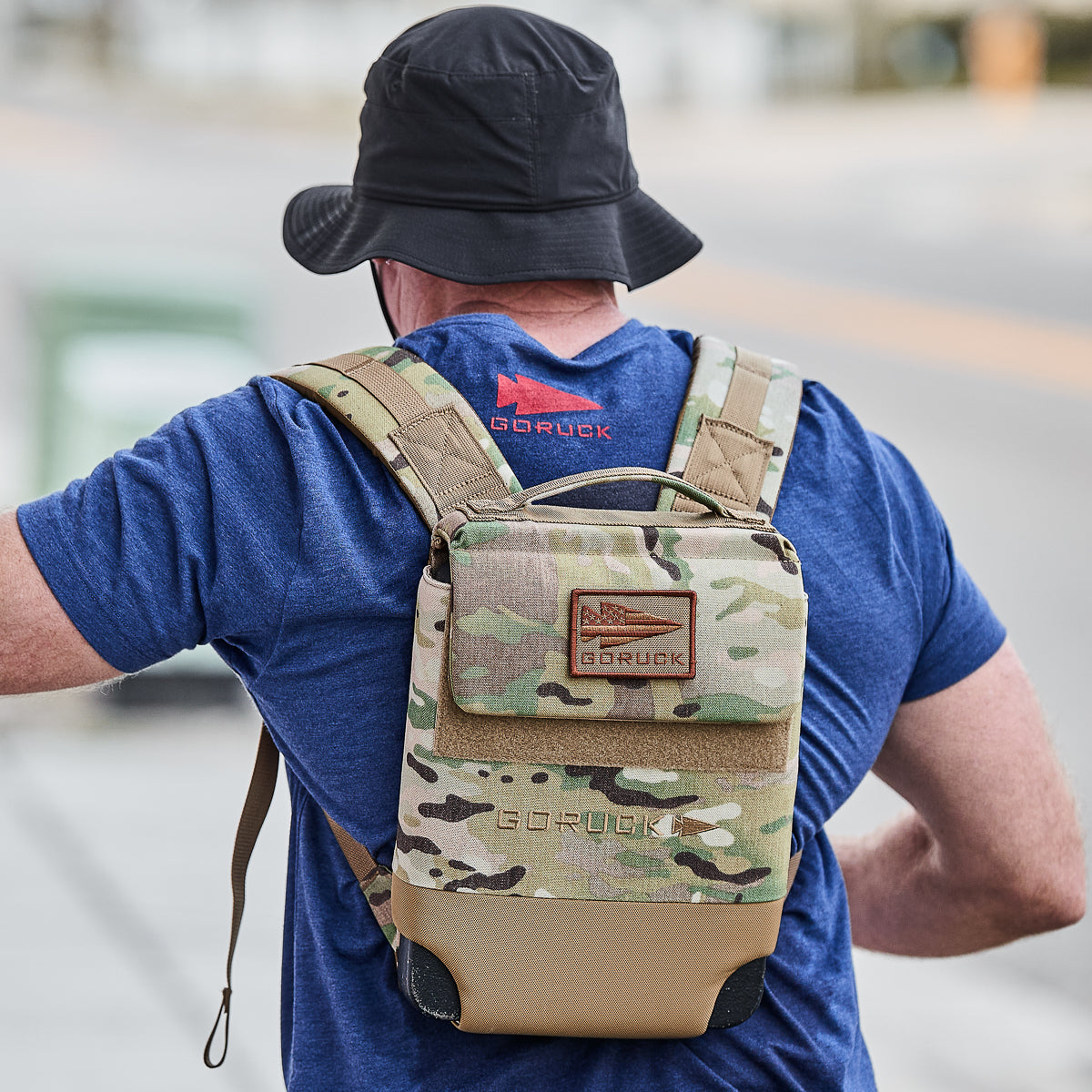 Man wearing GORUCK navy tee and camouflage backpack outdoors, rucking gear focus