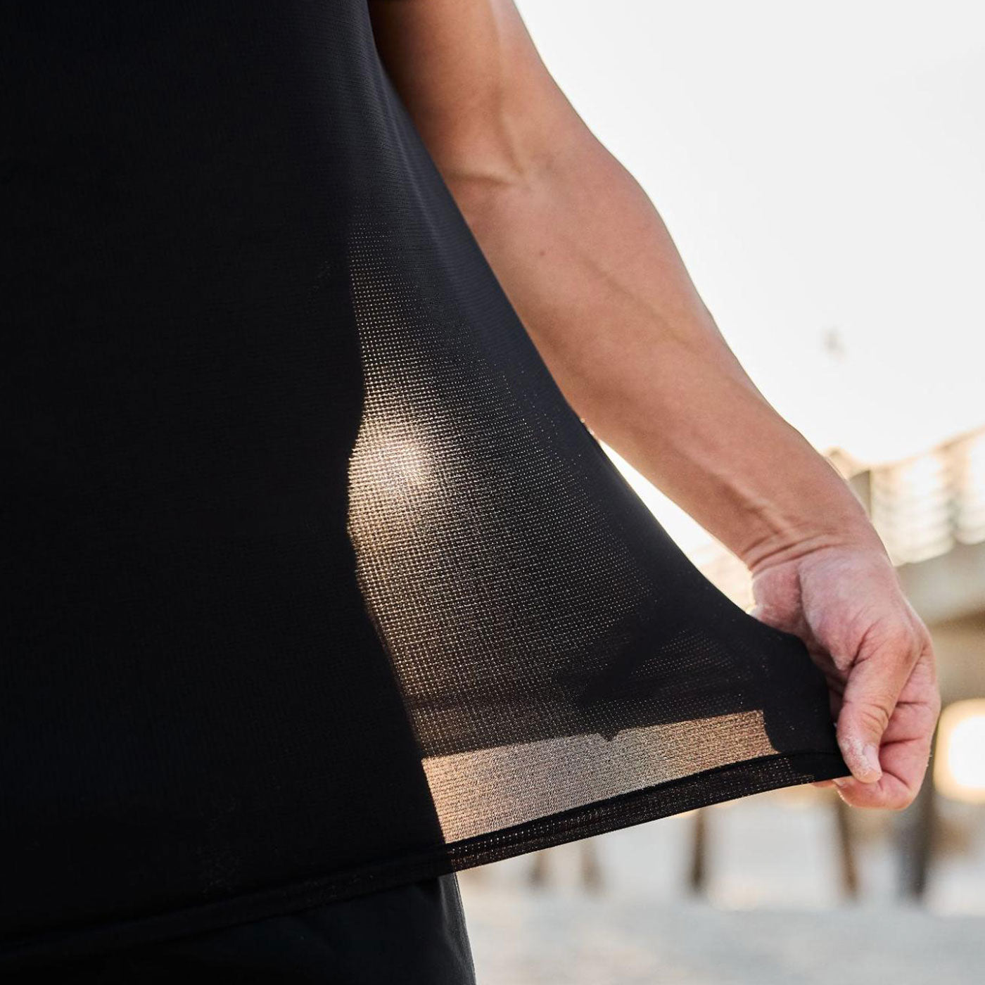 A person holds out a sheer black shirt, sunlight shining through the lightweight fabric.