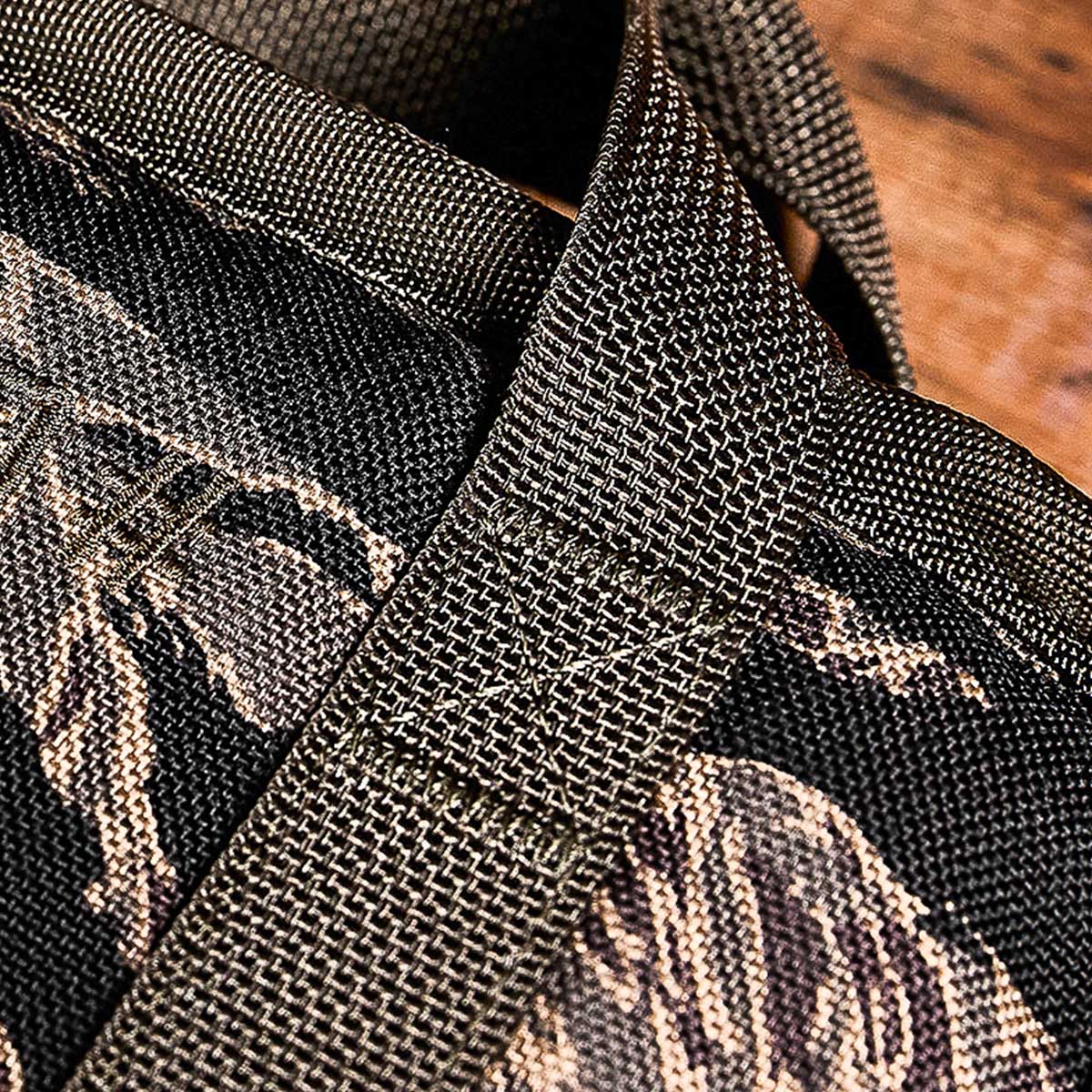 Close-up of a textured, brown strap stitched onto a dark, patterned fabric background.