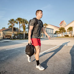 Man rucking outdoors with GORUCK backpack and gym bag, wearing athletic gear