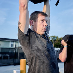 Man lifting weighted ruck over head outdoors in GORUCK workout gear