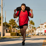 Man rucking outdoors in GORUCK gear, wearing red GORUCK shirt and black shorts on city street