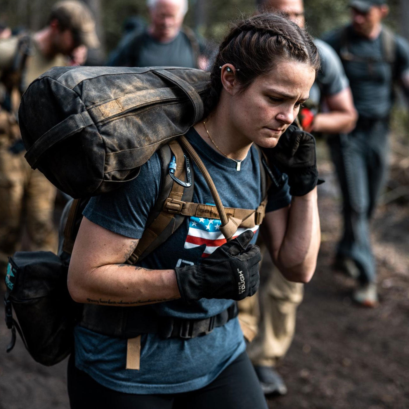 A woman carrying a heavy backpack and wearing gloves walks outdoors with a group of people.
