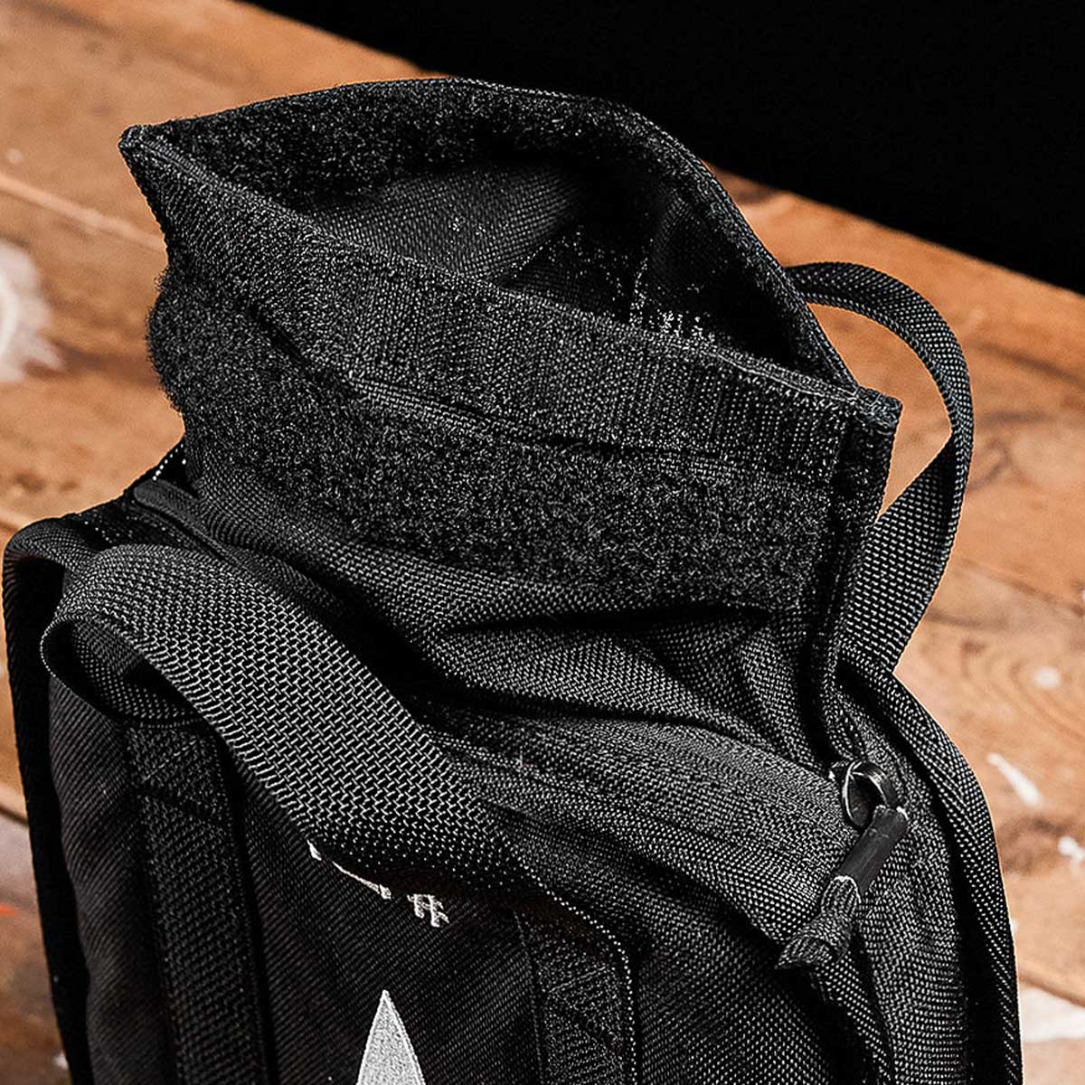 A close-up of a black fabric bag with a zipper and hook-and-loop fastener on a wooden surface.
