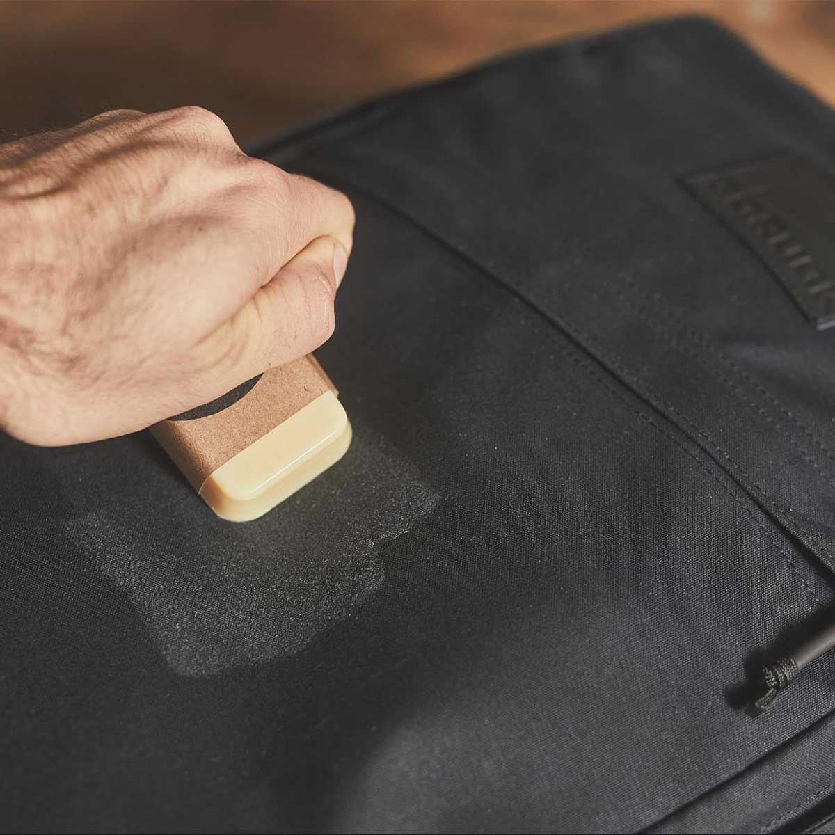 Hand applying a wax bar to a black fabric bag for waterproofing or maintenance.