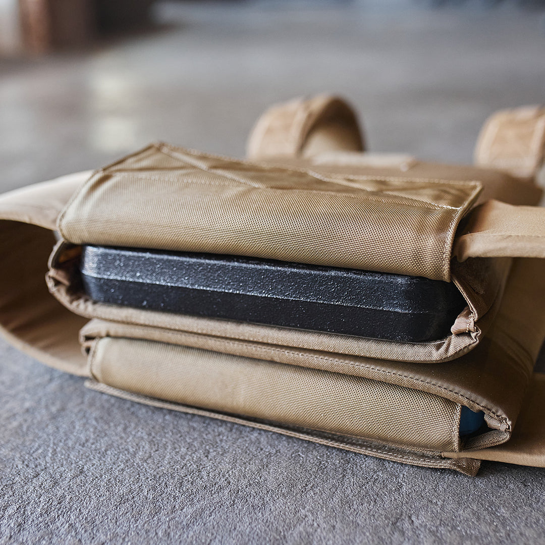 Close-up of a ballistic plate inserted into a GORUCK Training Weight Vest 2.0, shown on a concrete floor.