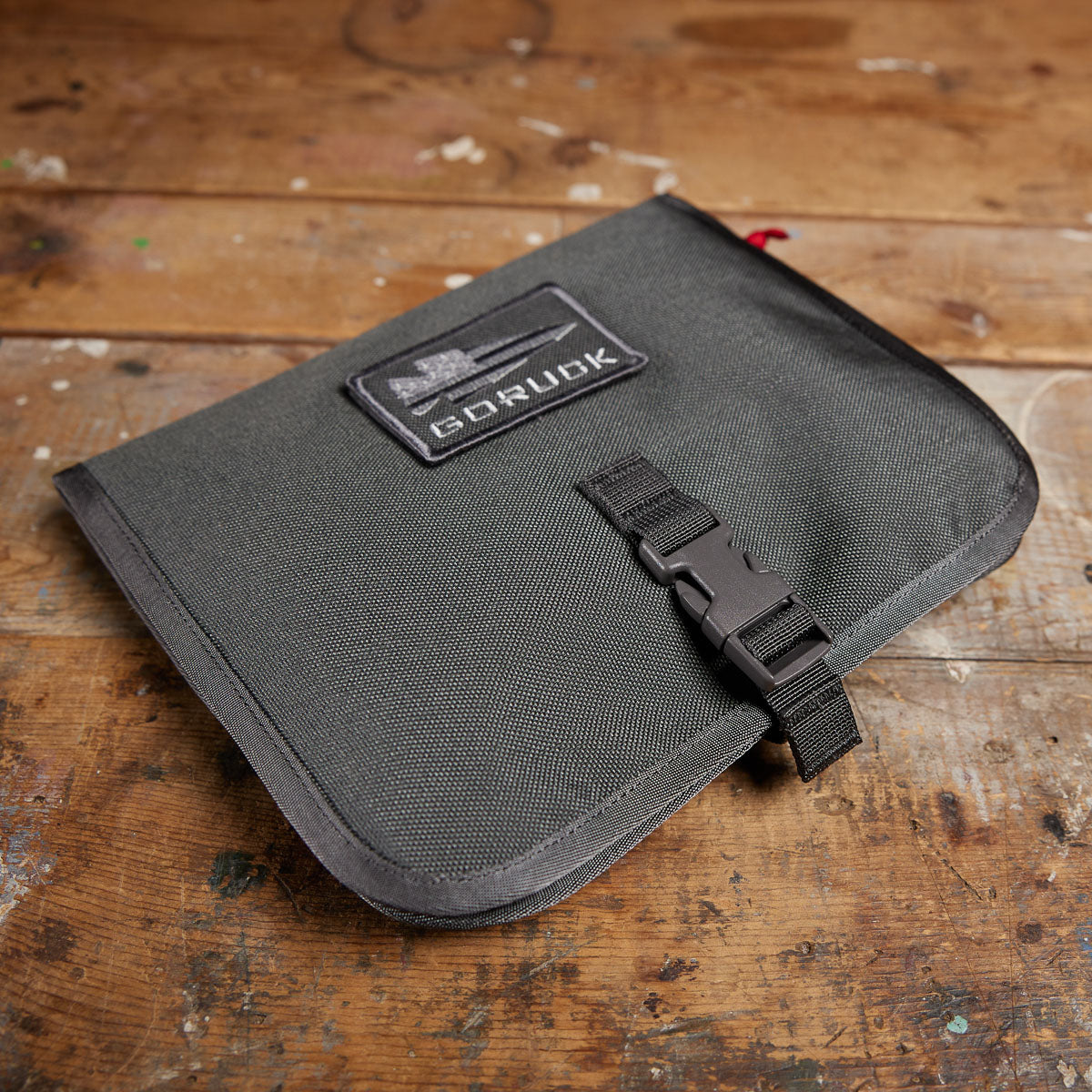 The GORUCK Wire Dopp, crafted from rugged black CORDURA and featuring a buckle, rests on a worn wooden surface—ideal for keeping your travel essentials organized.