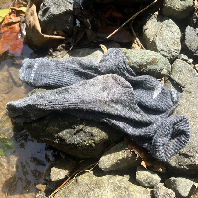 A pair of gray socks lying on rocks beside a small stream or shallow water.