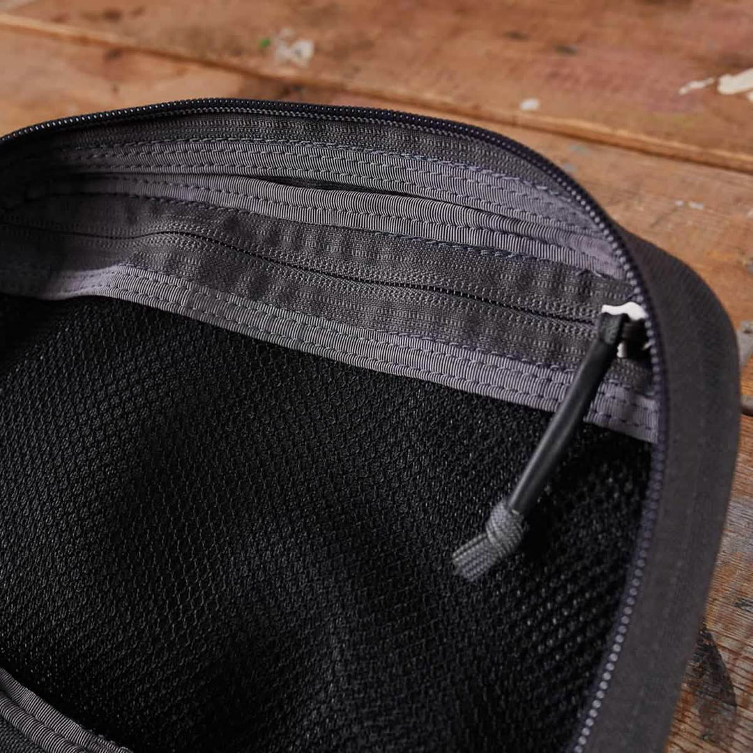 The GORUCK GR1 Field Pocket, shown open on a wooden surface with its black mesh zippered interior and pull, is ideal as a compact dopp kit or electronics organizer.