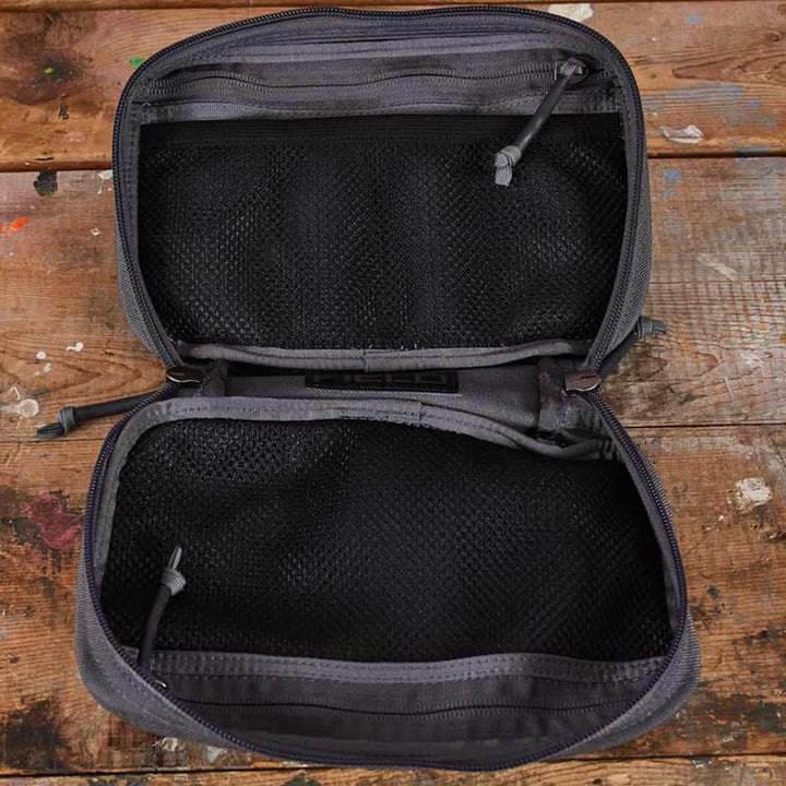 A black GORUCK GR1 Field Pocket, ideal as an electronics organizer or dopp kit, sits open and empty on a worn wooden surface.
