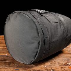 The GORUCK Brick Bag (5-50 LBS), a black cylindrical duffel perfect as a versatile stuff sack for ruck training or use with GORUCK gear, sits on a wooden surface against a black background.