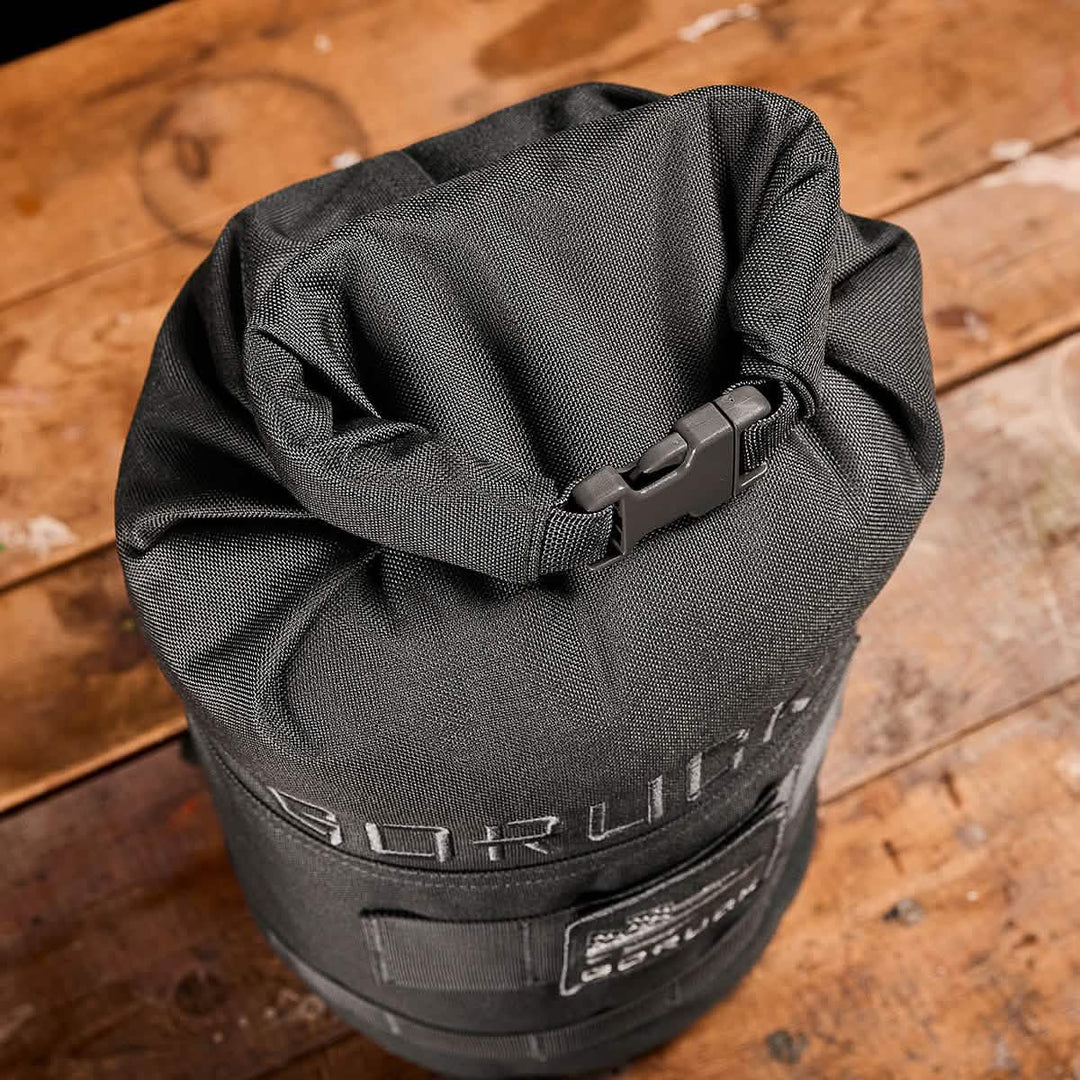 A GORUCK Brick Bag (5-50 LBS) in black with a buckle rests on a worn wooden surface.