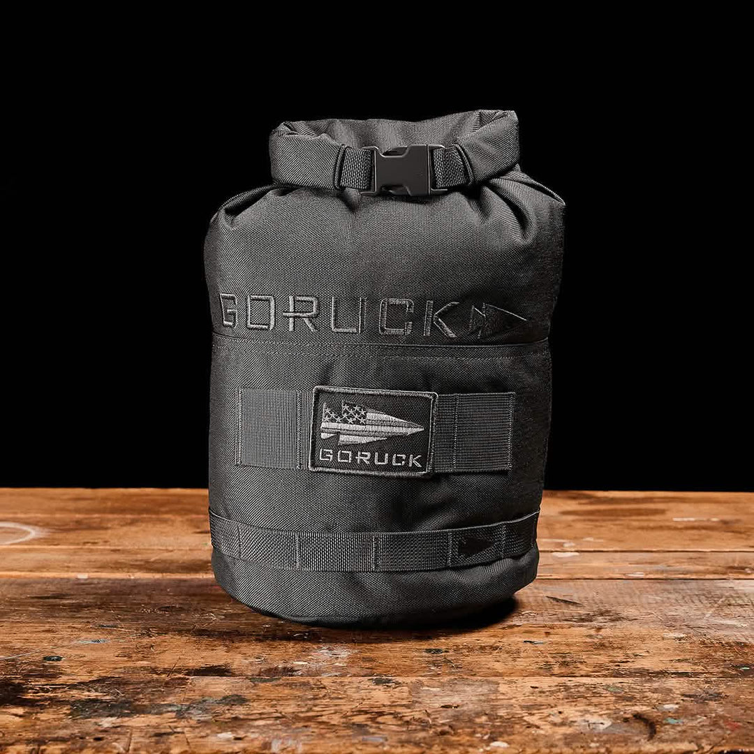 A GORUCK Brick Bag (5–50 LBS) in black rests on a wooden surface, displaying its patch and logo.