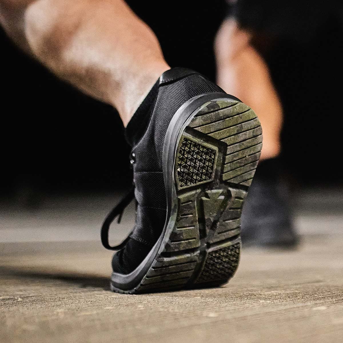 Close-up of a person wearing a black athletic shoe, focusing on the textured sole while walking or running.