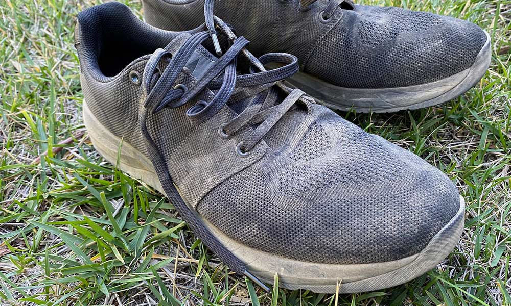 A pair of worn black sneakers with loose laces resting on green grass.