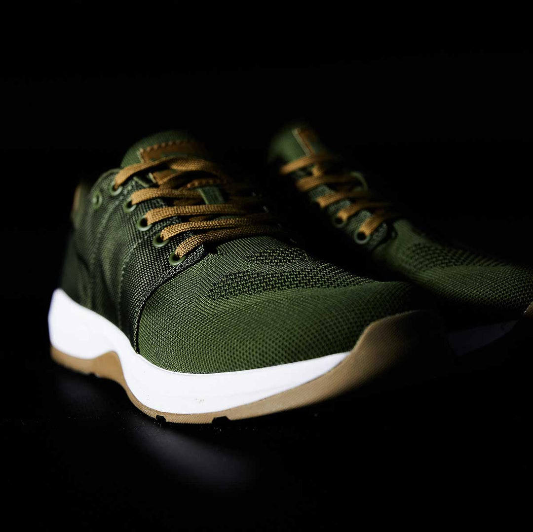 The GORUCK Ballistic Trainers – Green + White + Gum feature durable CORDURA® Ballistic Nylon, brown laces, and white soles, designed for functional fitness. Shown against a black background.