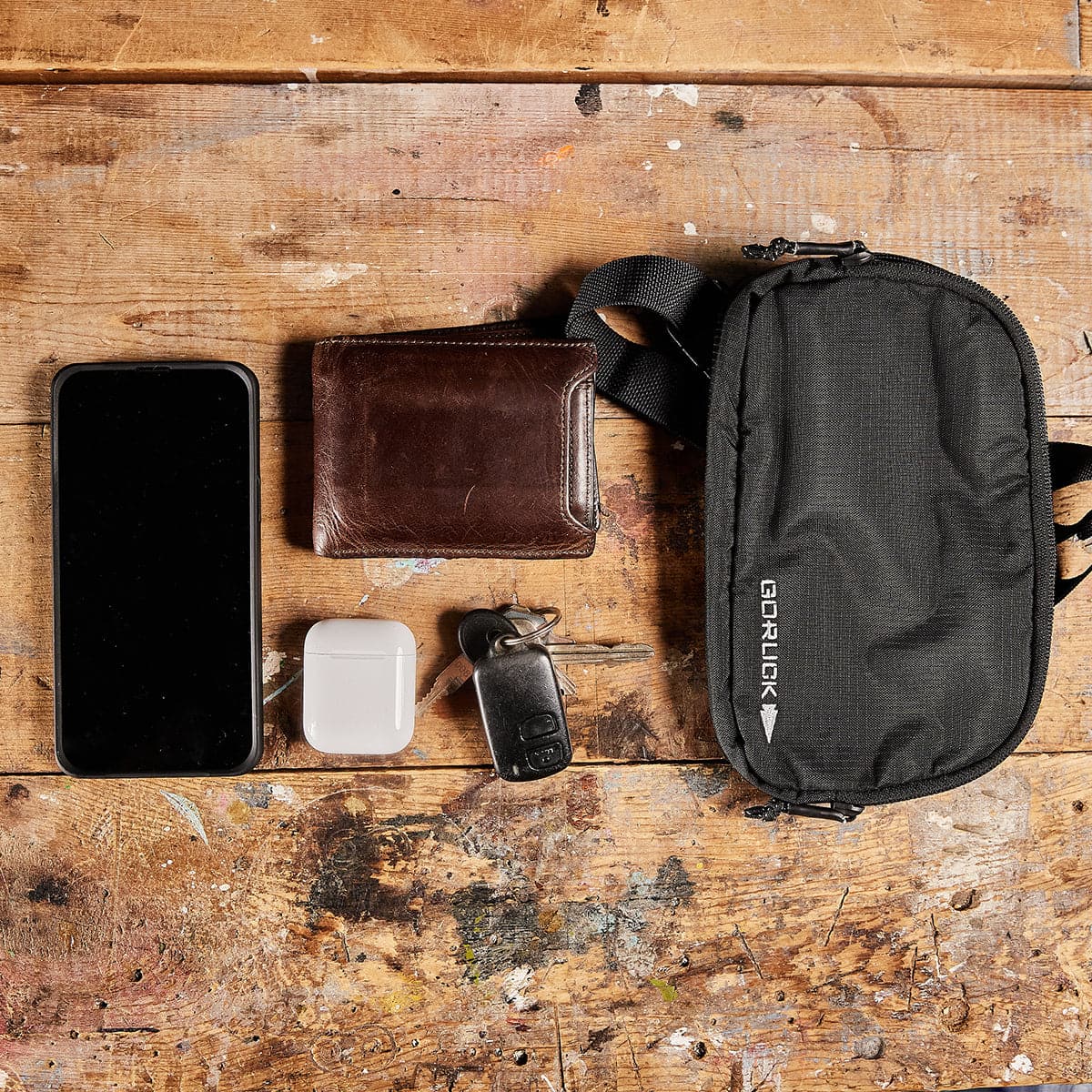 GORUCK belt bag on wooden table with phone, wallet, AirPods, and keys, everyday carry gear