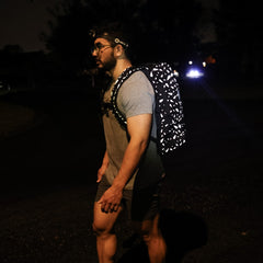 A person carrying a reflective Rucker 4.0 backpack by GORUCK and using a headlamp, lighting up the dark street as they ruck at night.