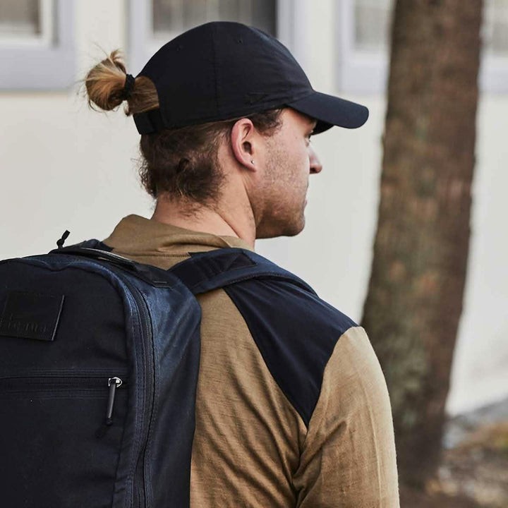 Man wearing GORUCK black rucksack and black cap outdoors, ready for rucking activity