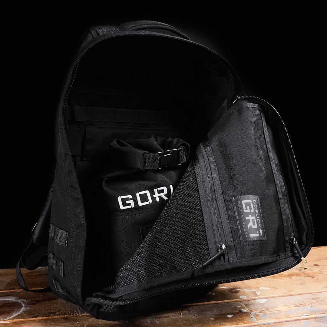 A GORUCK Brick Bag (5-50 LBS) lies unzipped on a wooden surface, revealing an organized interior—perfect for storing military gear or pairing with a stuff sack.