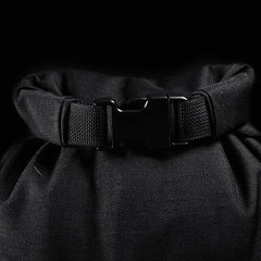 Close-up of a GORUCK Brick Bag (5-50 LBS) in black fabric with a plastic buckle clip, reminiscent of military gear, set against a black background.
