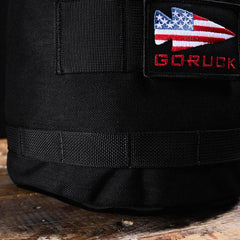 Close-up of a GORUCK Brick Bag (5-50 LBS) in black, featuring a patch with a US flag arrow and "GORUCK" in red, inspired by classic military gear.
