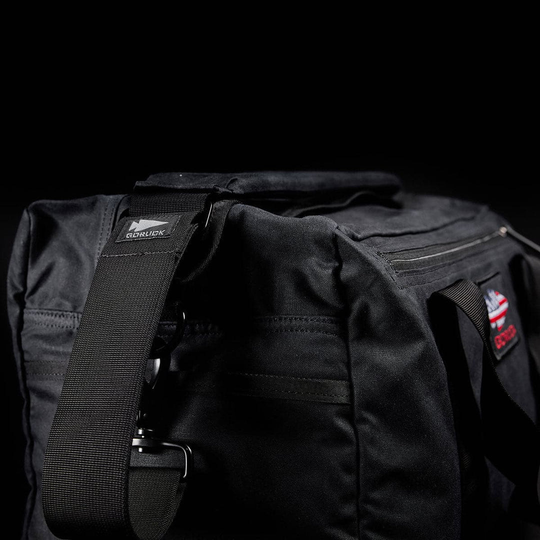 Close-up of a black Kit Bag - Waxed Canvas by GORUCK with a shoulder strap, set against a dark background.
