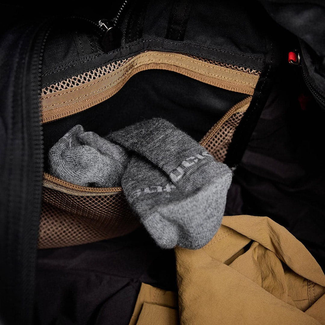 Open the GORUCK Kit Bag - Waxed Canvas to reveal a pair of gray socks nestled in a mesh pocket, with a tan fabric item below.