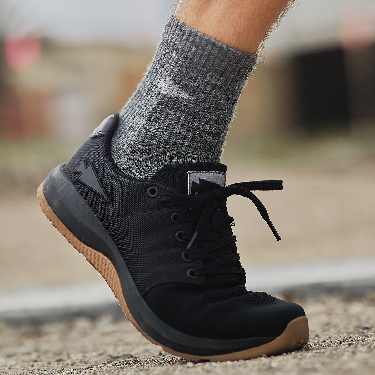 A person wearing gray socks and black athletic shoes standing on a gravel surface.