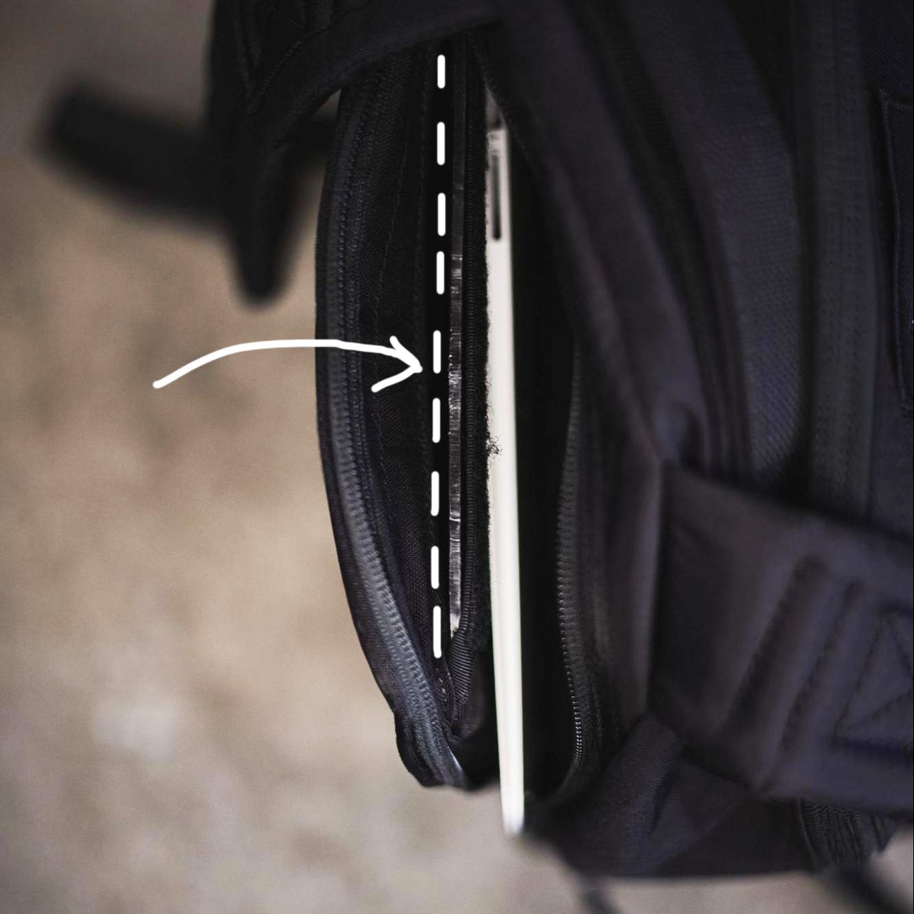 A laptop partially tucked in a black backpack, indicated by a white dashed line and arrow.