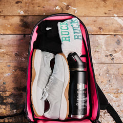 Open gym bag with sneakers, socks, a water bottle, and gym clothes neatly packed alongside a compact 15L Bullet Ruck - Classic by GORUCK on a wooden floor.
