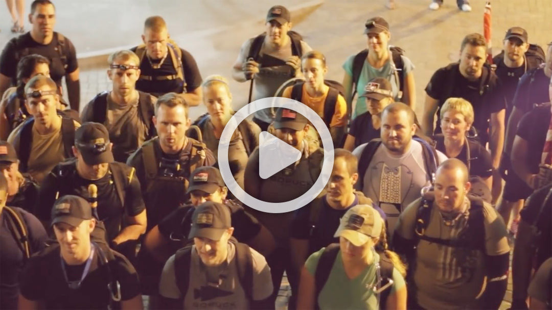 A group of people with backpacks stand closely together, looking up, outdoors at night.
