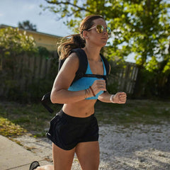 Woman running outdoors wearing GORUCK backpack, athletic shorts, and blue top