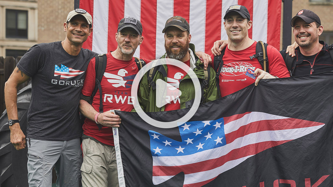 Five men smile in front of an American flag, holding a black flag with a stylized American flag design.