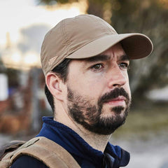 Man wearing tan GORUCK rucking cap outdoors, close-up with backpack strap visible
