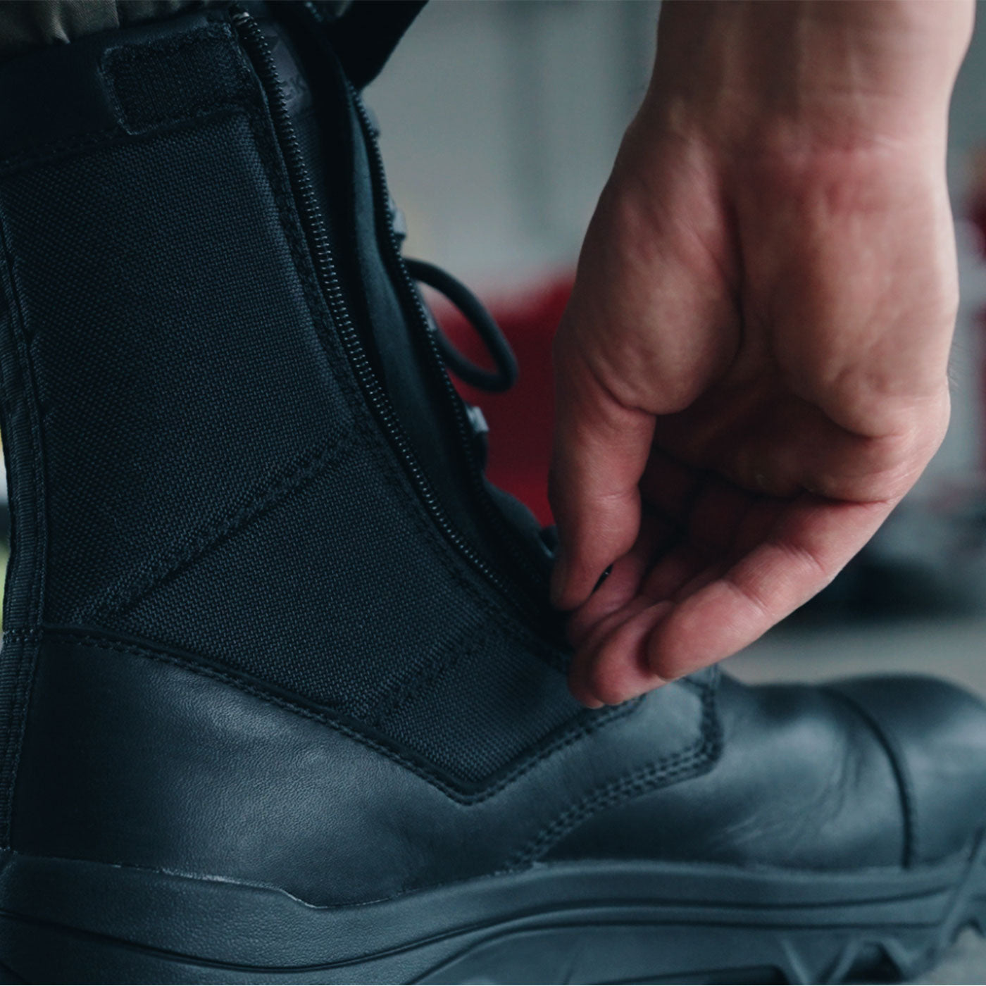 A hand zipping up a black combat boot.