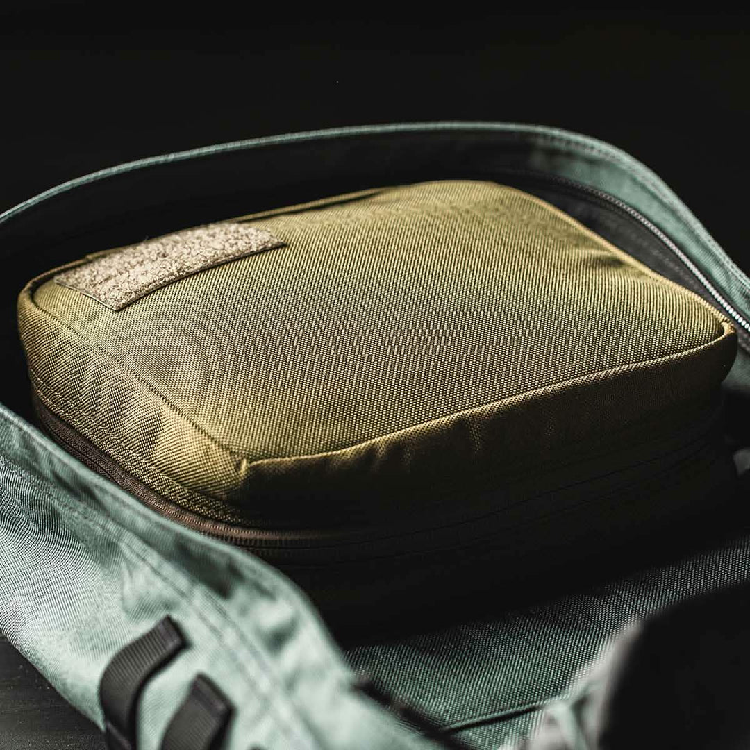 A close-up of the green GORUCK GR2 Field Pocket, used as an electronics organizer inside an open backpack.