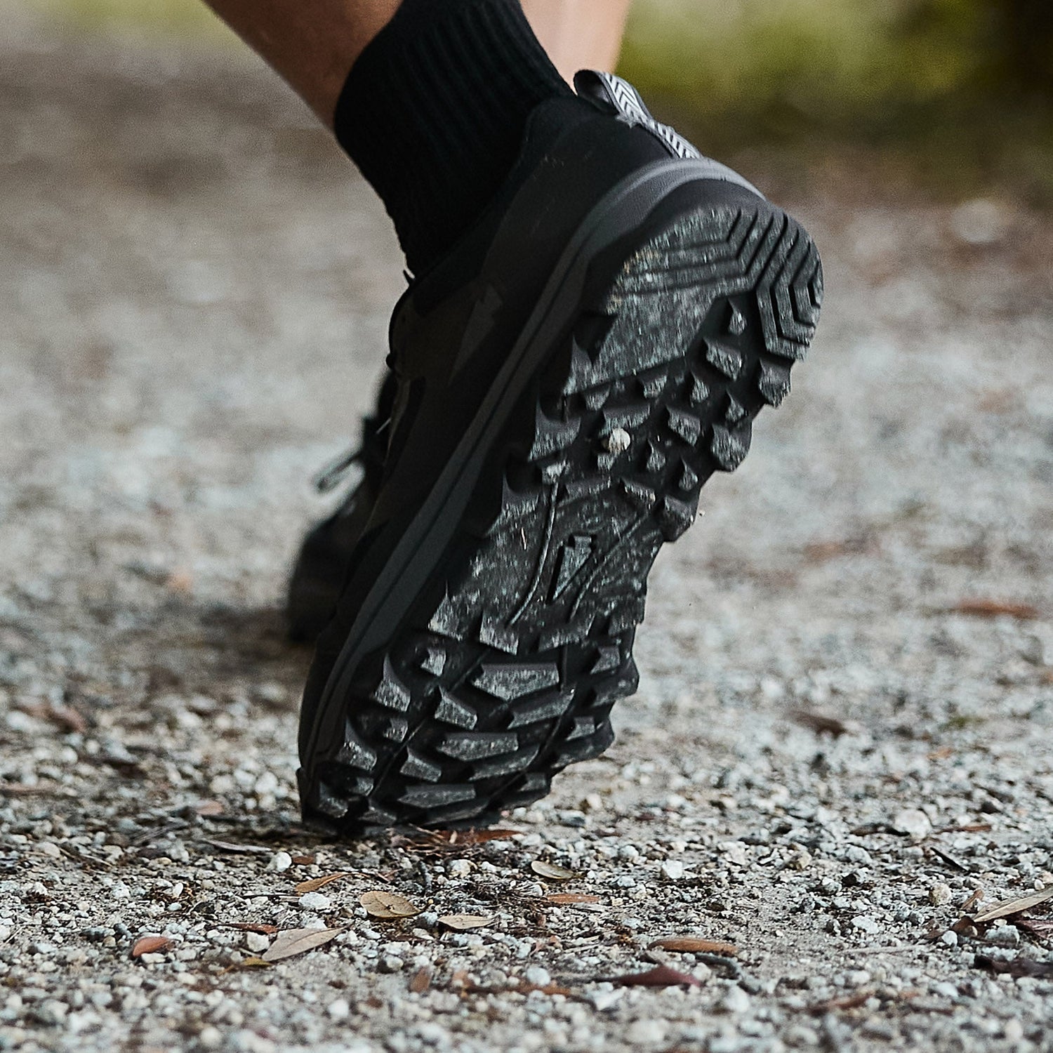 Close-up of a person’s black trail shoe stepping on a gravel path outdoors.