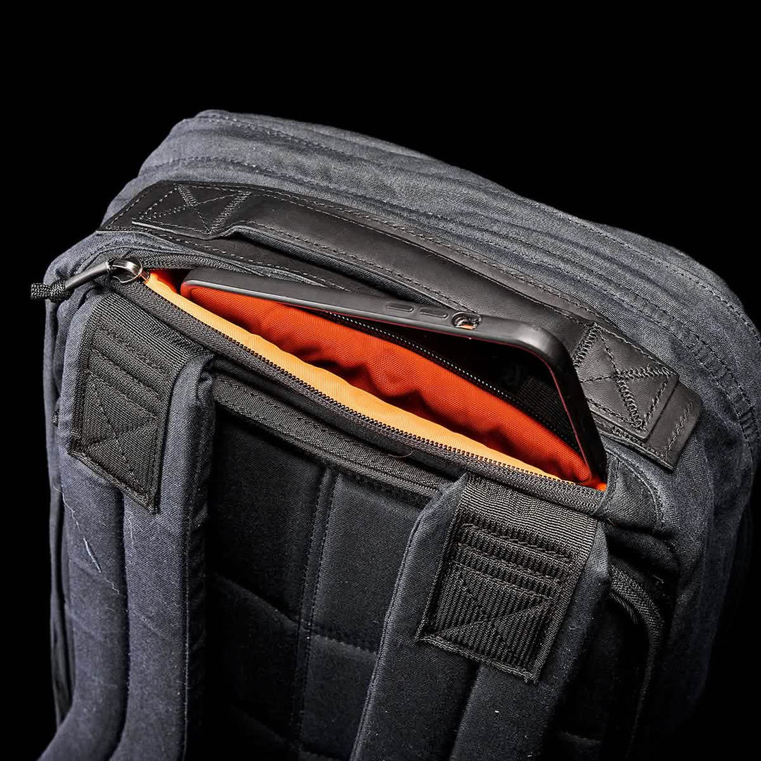 The GR1 USA - Heritage by GORUCK is a partially open black rucksack with an orange interior and a tablet inside, crafted in sleek waxed canvas for durability and style.